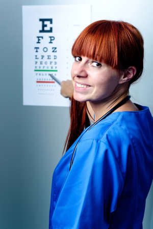 female oculist doctor examining patient with an eye chart behindの写真素材