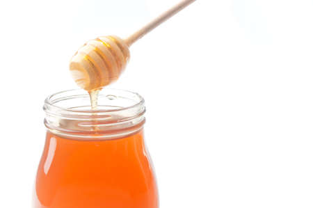 Jar of honey with wooden drizzler isolated on white backgroundの写真素材