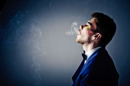 Dark portrait of the young beautiful man. The young man smokes cigaretteの写真素材