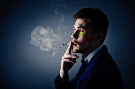Dark portrait of the young beautiful man. The young man smokes cigaretteの写真素材