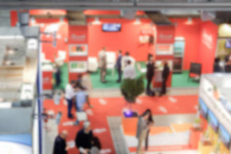 Defocused background of a trade show with people visiting the commercial exhibition. Intentionally...