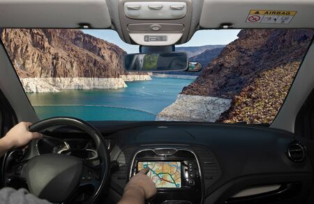 Driving a car while using the touch screen of a GPS navigation system with view of Colorado river in front of the Hoover Dam on the Nevada side, USAの写真素材
