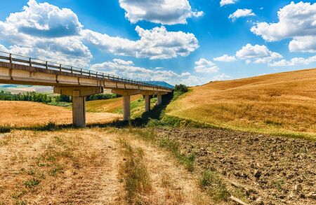 Highway crossing a landscape of dry fields in the countryside in Tuscany, Italy. Concept for agriculture and farmlandsの写真素材