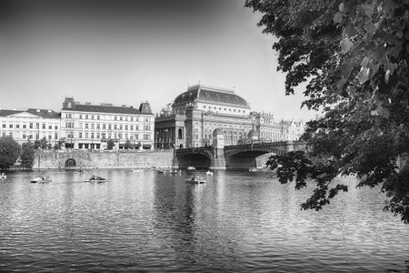 The National Theater sitting on the bank of the Vltava river in Prague with tourists enjoying a sunny day on paddle boatsの写真素材