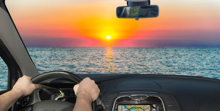 Driving a car towards a scenic sunset on the Mediterranean sea at the end of summerの写真素材