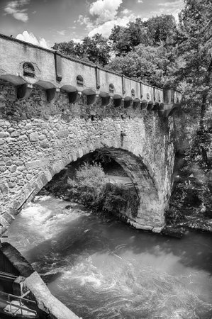 View of Steinerner Steg bridge crossing a river with lush green trees on both sides, iconic landmark in Merano, South Tyrol, Italyの写真素材