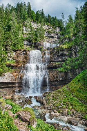 Water is cascading down the rocky mountainside at Vallesinella Falls in the Dolomites mountain range in Italyの写真素材