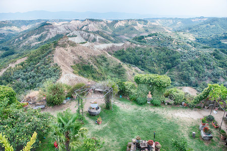 A wide-angle view reveals the unique eroded 'calanchi' badlands landscape near Civita di Bagnoregio, characterized by dry, light-colored soil and contrasting green vegetation under a cloudy sky.の写真素材