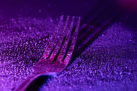 Single fork with waterdrops, in the dark illuminated with colourful gradient LED light.の写真素材