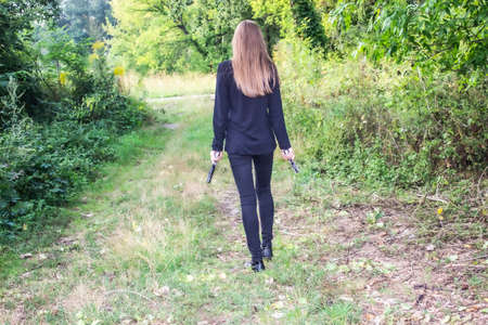 A Girl in black with a gun in the nature.  Agent. Long hair.の写真素材