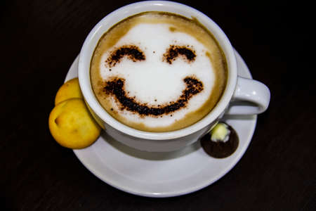 the cup of coffee with smile on the table. The biscuits with candy. Smile. Be happy with coffe