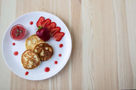 Three pancakes with cheese and strawberries and sauce on a white dish against wood background. Delicious cheese pancake and strawberries for the breakfast or lunch. Tasty meal with berries.の写真素材