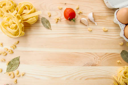 Cooking food background with free space for text. Composition with pasta, tomato, eggs, garlic, bay leaf over the wood background. Ingredients for cooking with copy space. Top view with copy spaceの写真素材