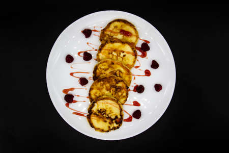 Ukrainian cottage cheese fritters, syrniki with jam on white plate. Cheese pancakes with raspberry...