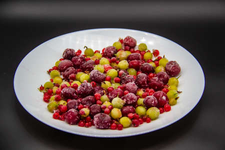 Frozen berries from the freezer. Plate with frozen cherries, currants and gooseberries. Healthy berry on a white plate.の写真素材