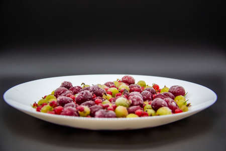 Frozen berries from the freezer. Plate with frozen cherries, currants and gooseberries. Healthy berry on a white plate.の写真素材