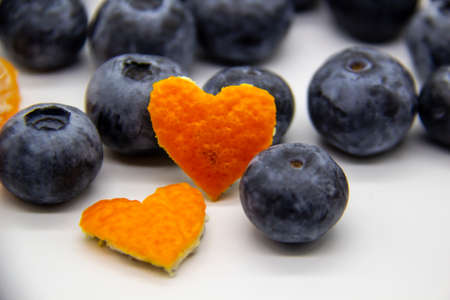 Fresh blueberry  with mandarin peel in form a heart on white background. A composition of the blueberries, mandarin peel which is organic and healthy. The berries full of vitamins.の写真素材