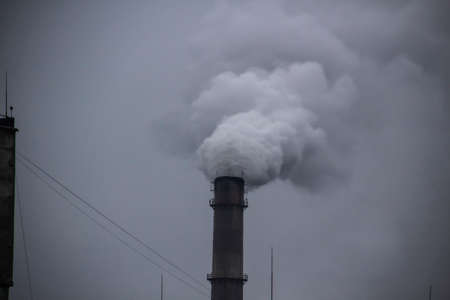 Industrial Smoke Pipe against grey sky. Industrial chimney fume mix in clouds. Smoke air emissions...