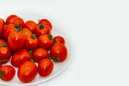Ripe fresh red cherry tomatoes on a white plate against white background.  Beautiful and healthy fresh cherry tomatoes without GMO. Copy space for text or designの写真素材