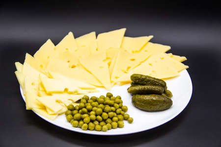 Beautiful plate with sliced ??cheese, cucumbers and green peas isolated on a dark background. Keto diet with very healthy and tasty meal for lunchの写真素材