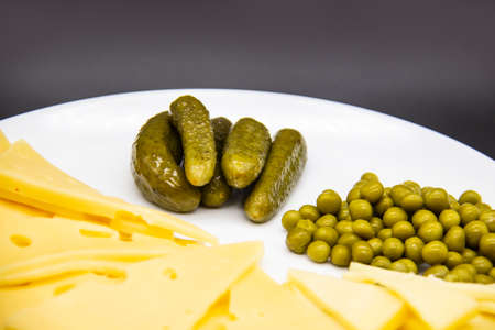 Beautiful plate with sliced ââcheese, cucumbers and green peas isolated on a dark background. Keto diet with very healthy and tasty meal for lunchの写真素材