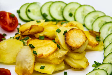 Homemade fried potatoes with fresh cucumbers, cherry tomatoes and sauces on the white plate. Delicious ukrainian fried potatoes with vegetables against background. Cooked tasty meal for lunch.の写真素材