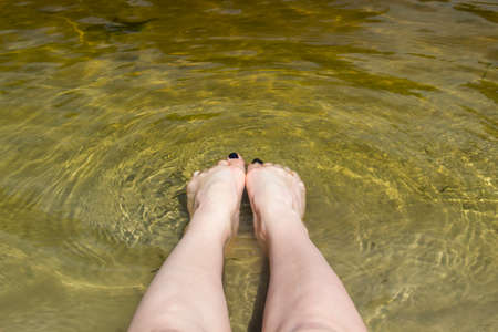 Feet girl in the river with black nails from pedicure. Female legs is relaxing in the water of the riverの写真素材