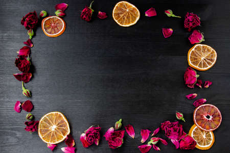 Wooden background with dry roses and petals and slices of dry orange with copy space. Flat lay composition with frame border made of dry roses and citrus.の写真素材