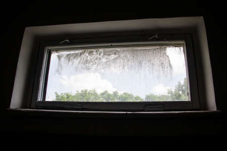 A dirty window from a dark gloomy room and a light from outside. Old shabby window with dirty glass, the dark walls and the light from outsideの写真素材