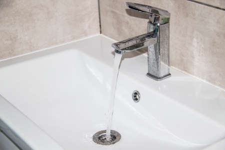 Water runs from the tap into the sink. Modern water tap in the bathroom with running flowing water...