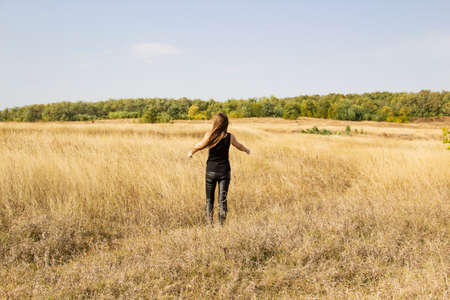 Beautiful young dark haired woman in black clothes stand in field.