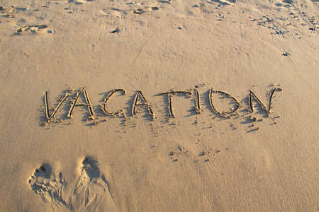 Word VACATION wrote on the sand against background. Message says "vacation" in the sand on the beachの写真素材