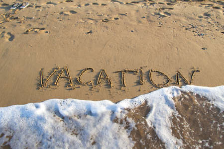Word VACATION wrote on the sand against background. Message says vacation in the sand on the beach...