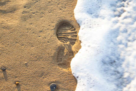 Sea foam from a wave on the sand with traces. Human footprint on the sand with sea water.の写真素材
