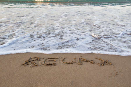 Word RELAX wrote on the sand against background. Message says "relax" in the sand on the beach with sea foamの写真素材