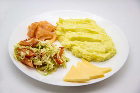 Tasty breakfast or lunch with potato puree with fresh salad with cabbage and tomatoes, cucumber and red fish - salmon, and pieces of cheese on the white plateの写真素材