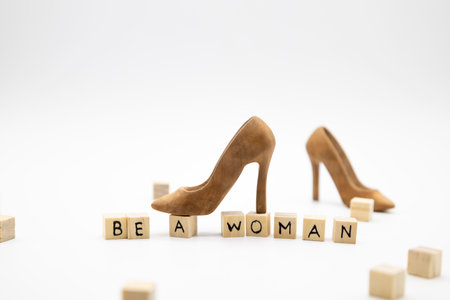 A beautiful high-heeled wooden shoe stand on wooden cubes with the inscription BE A WOMAN against white background. Concepts for the female design.の写真素材