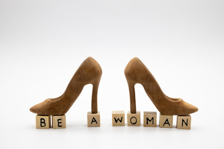 A beautiful high-heeled wooden shoes stand on wooden cubes with the inscription BE A WOMAN against white backgroundの写真素材