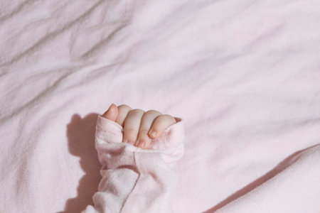 A tiny hand with delicate fingers wrapped in soft white fabric against a white backgroundの写真素材