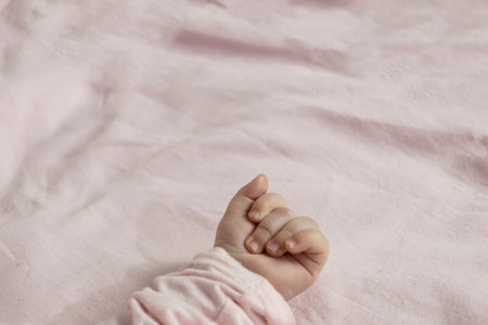 A tiny hand with delicate fingers against a soft pink background