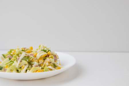 Tasty and healthy salad with cabbage, cucumber, corn, ham and mayonnaise on a white plate.の写真素材