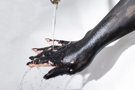 Concept photo with the painted hand. The black hand with long nails clean paint with water from tapの写真素材
