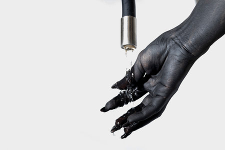 Concept photo with the painted hand. The black hand with long nails clean paint with water from tapの写真素材