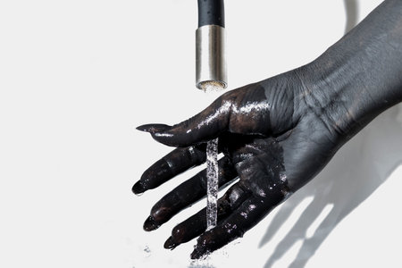 Concept photo with the painted hand. The black hand with long nails clean paint with water from tapの写真素材