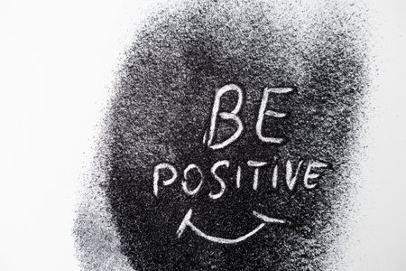 On the black glitters drawing words BE POSITIVE and the smile white background. Abstract minimalist composition from glitterの写真素材