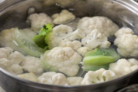 Fresh cauliflower is boiled in a saucepan with water. The vegetable is divided into florets and boiled in a saucepan.の写真素材