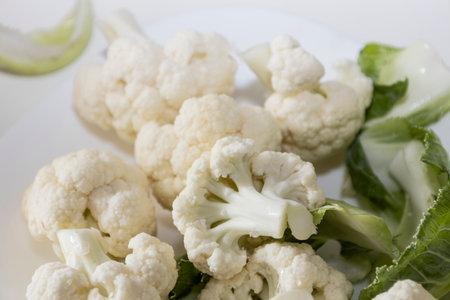 Fresh and raw cauliflower on the white plate. The cauliflower - vegetable is cut into pieces on white background. The vegetable is divided into inflorescences on the plateの写真素材