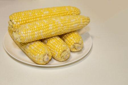 Raw cobs of sweet corn on plate against background. Tasty sweet corn on cobs