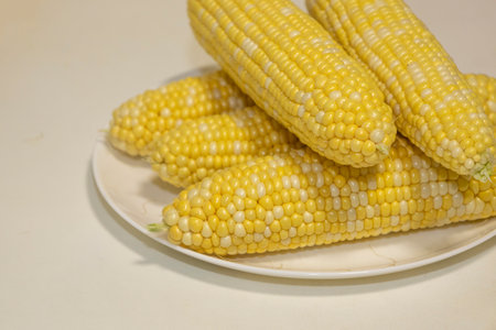 Raw cobs of sweet corn on plate against background. Tasty sweet corn on cobs