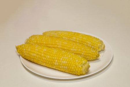 Three cooked cob of sweet corn on white plate against background. Tasty sweet corn on cob.
